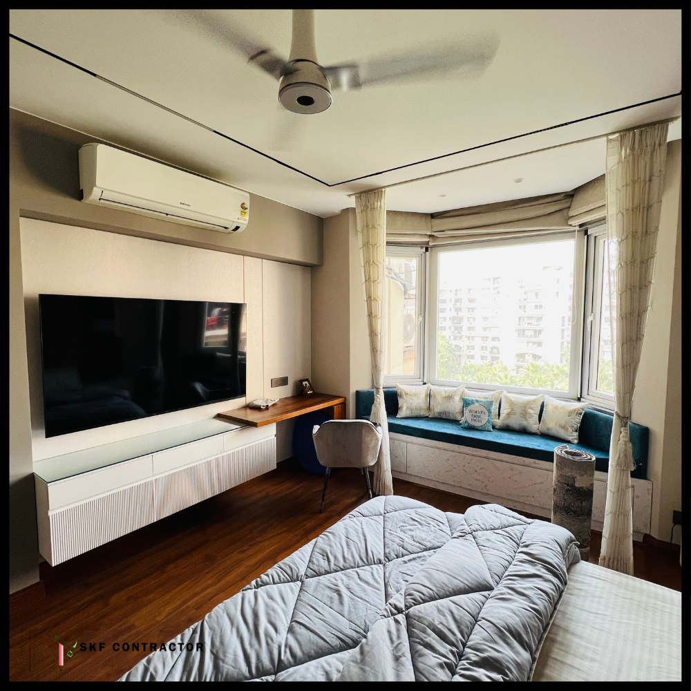 Bedroom TV unit with fluted white cabinet, wooden study ledge and teal window seating.