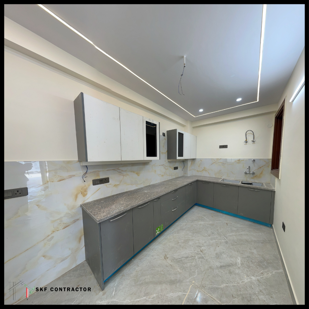 L-shaped modular kitchen with grey cabinets, marble backsplash and LED ceiling lighting.
