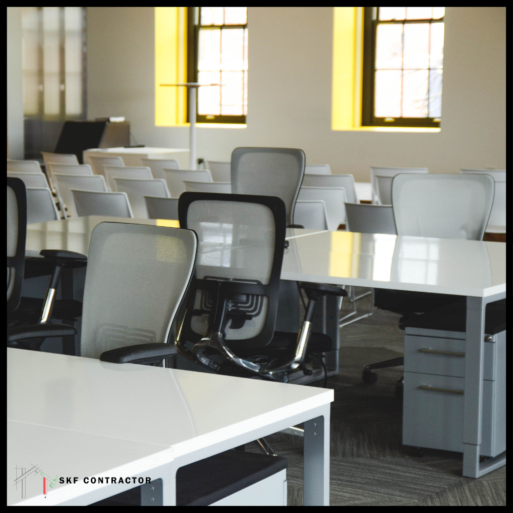 Open-plan office with white workstations, mesh chairs, drawer pedestals, and yellow grid windows.